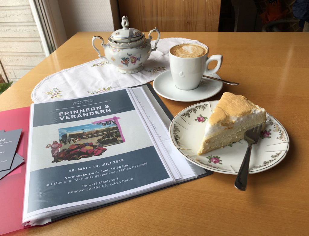 Ausstellungsmappe "erinnern & verändern" mit Cappuccino und einem Stück Kuchen im Café Mahlsdorf