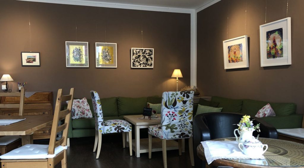Ausschnitt vom Café Mahlsdorf, Sofaecke mit Bildern darüber von Doreen Trittel