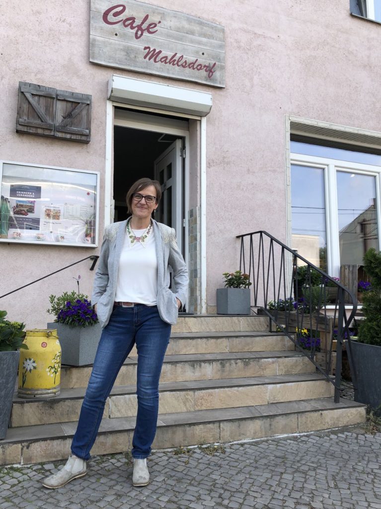 Die Künstlerin Doreen Trittel steht vorm Café Mahlsdorf mit ihrer Ausstellung, Collagen